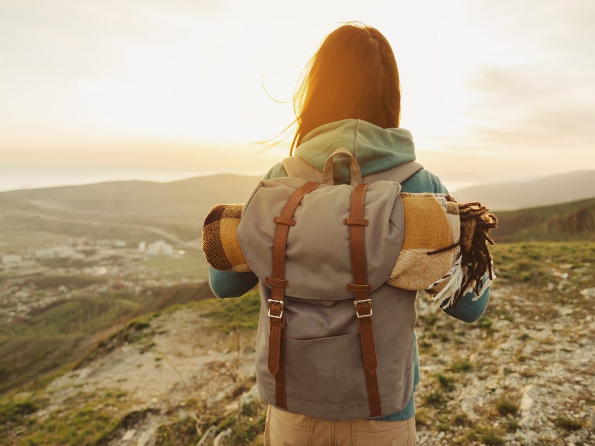 Hiker woman with backpack and sleeping bag walking in the mountains in summer at sunset